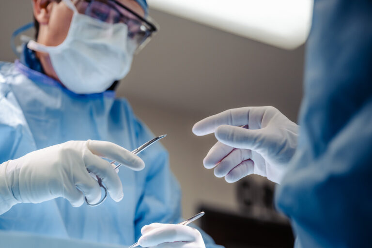 Surgeon passing a surgical tool to a coworker while performing a joint replacement surgery in KC.